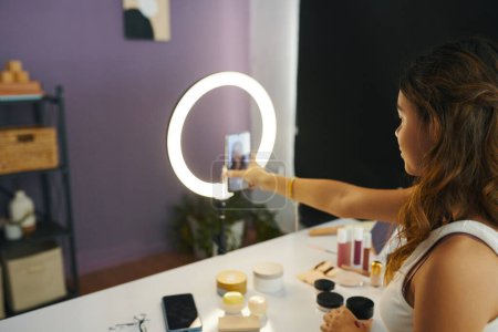 Foto de Adolescente adjuntando un teléfono inteligente a la luz del anillo para filmar su maquillaje diario - Imagen libre de derechos