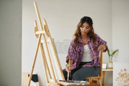Photo for Creative zoomer girl in plaid shirt painting picture on canvas - Royalty Free Image
