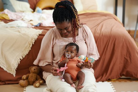 Foto de Negro mujer sentado en piso y jugando con bebé chica chupando chupete - Imagen libre de derechos