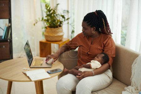 Foto de Mujer negra con bebé recién nacido trabajando en la computadora portátil en casa - Imagen libre de derechos