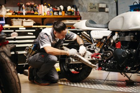 Photo for Mechanic in uniform concentrated on diagnosing and fixing common problems with motorcycle - Royalty Free Image