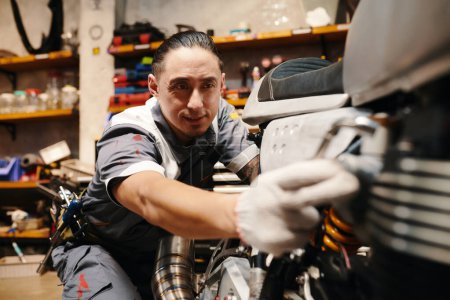 Téléchargez les photos : Mécanicien expérimenté en uniforme réparation de moto dans le garage, concept de petite entreprise - en image libre de droit