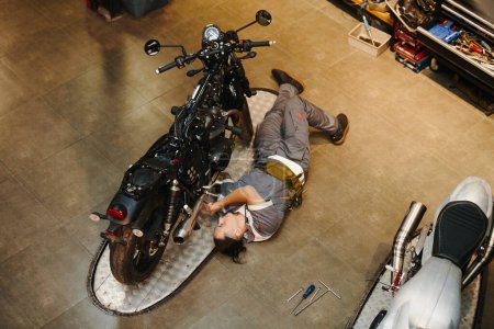 Photo for Mechanic lying next to motorcycle when repairing vehicle - Royalty Free Image