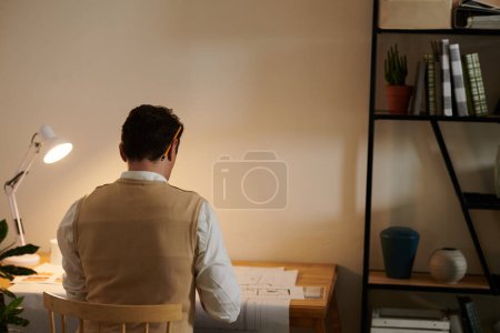 Téléchargez les photos : Architecte travaillant au bureau dans le bureau sombre avec un crayon derrière l'oreille - en image libre de droit