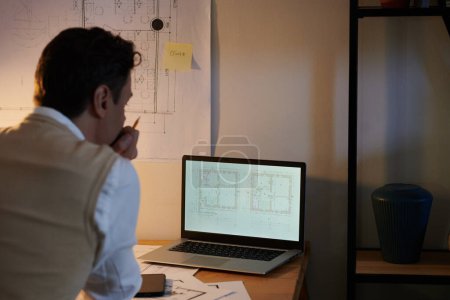 Téléchargez les photos : Architecte pensif regardant le plan de l'appartement sur l'écran d'ordinateur portable - en image libre de droit