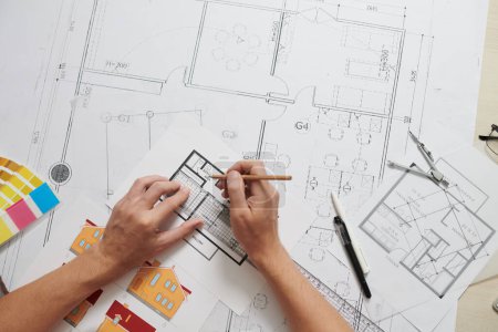 Téléchargez les photos : Mains de l'architecte corrigeant le plan de l'appartement à son bureau, vue d'en haut - en image libre de droit