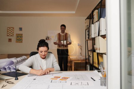 Téléchargez les photos : Femme architecte mature travaillant sur le plan de construction quand collègue apportant sa tasse de café à emporter - en image libre de droit