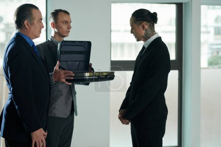 Photo for Assistant of entrepreneur showing content of briefcase to businessman at meeting - Royalty Free Image