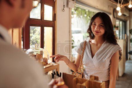 Téléchargez les photos : Jeune femme souriante achetant des croissants frais dans le coffeeshop pour le petit déjeuner - en image libre de droit