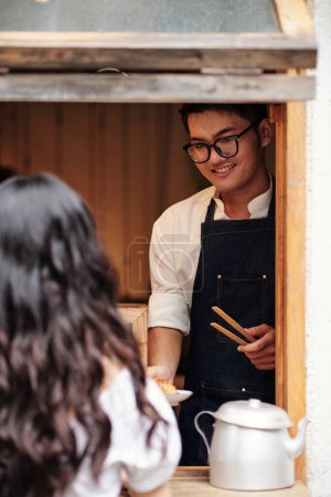 Photo for Smiling young Asian barista giving order to female customer - Royalty Free Image