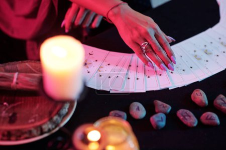 Photo for Closeup image of fortune teller predicting fate with tarot cards in darl room with burning candles - Royalty Free Image