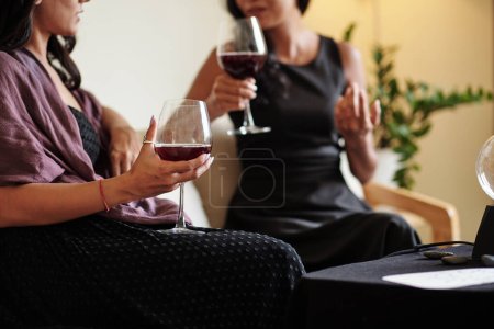 Téléchargez les photos : Jeune femme avec du fil rouge au poignet qui aide à éviter le malheur en buvant du vin et en parlant à un meilleur ami - en image libre de droit