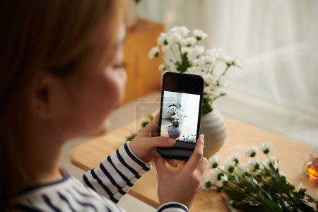 Téléchargez les photos : Image rapprochée de jeune femme photographiant des fleurs de marguerite dans un vase sur smartphone - en image libre de droit