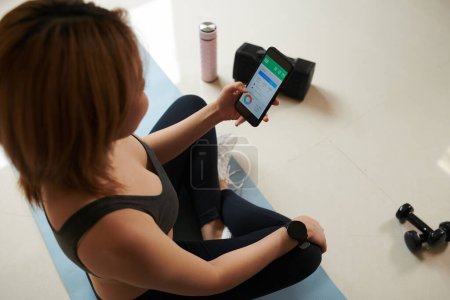 Photo for Fit young woman checking her activity statistics in mobile application after training at home - Royalty Free Image