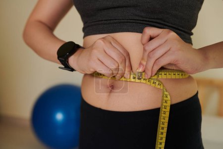 Téléchargez les photos : Image recadrée d'une jeune femme mesurant sa taille après un entraînement à la maison, un mode de vie sain et un concept de perte de poids - en image libre de droit