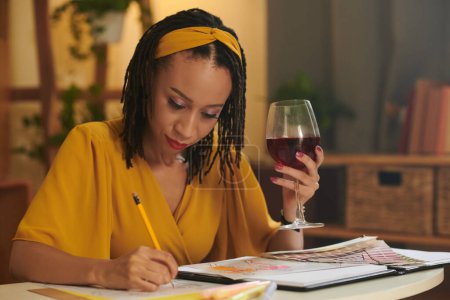 Photo for Creative Black woman drinking wine and drawing sketches for her fashion collection - Royalty Free Image