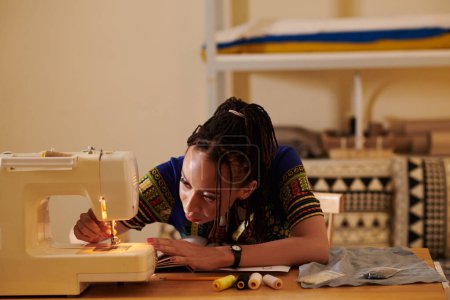 Foto de Costurera roscando la aguja de la máquina de coser cuando trabaja en su estudio - Imagen libre de derechos