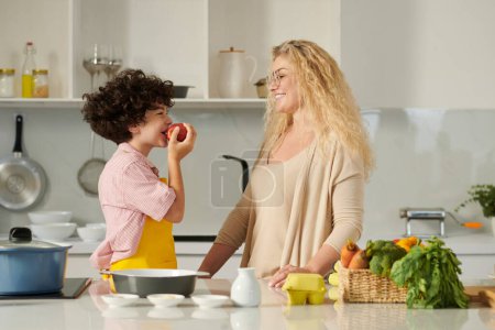 Foto de Mujer positiva mirando a su hijo teniendo manzana roja para merendar - Imagen libre de derechos