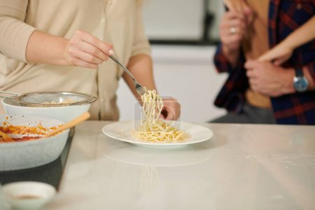 Téléchargez les photos : Image rapprochée de la femme mettant des pâtes dans des assiettes pour son mari et son fils - en image libre de droit