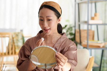 Téléchargez les photos : Portrait de jeune femme regardant miroir grossissant lors de l'application du maquillage - en image libre de droit