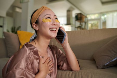 Téléchargez les photos : Jeune femme avec des patchs sous les yeux riant en parlant au téléphone avec un ami - en image libre de droit