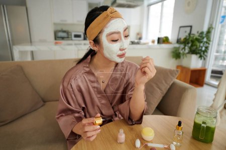 Foto de Mujer joven con mascarilla purificadora haciendo manicura en casa - Imagen libre de derechos