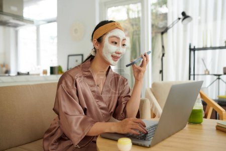 Photo for Cheerful young woman with face mask recording voice message for friend or colleague - Royalty Free Image