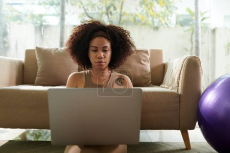 Téléchargez les photos : Femme latine sérieuse travaillant dans un ordinateur portable dans un salon ensoleillé - en image libre de droit