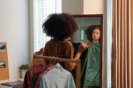 Téléchargez les photos : Femme essayant des vêtements en face du miroir de décider quoi porter pour le travail - en image libre de droit