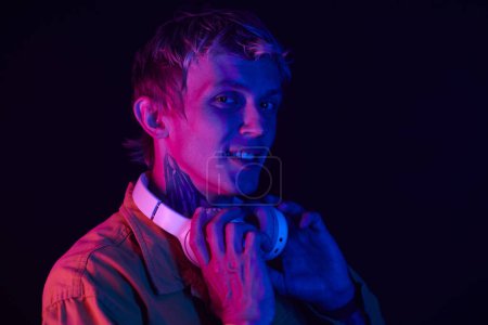 Téléchargez les photos : Portrait de club de nuit dj debout dans la lumière au néon et mettre des écouteurs - en image libre de droit