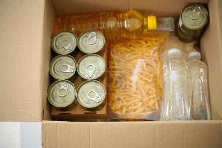 Téléchargez les photos : Viande en conserve, macaronis et bouteilles d'eau et d'huile végétale dans une boîte en carton - en image libre de droit