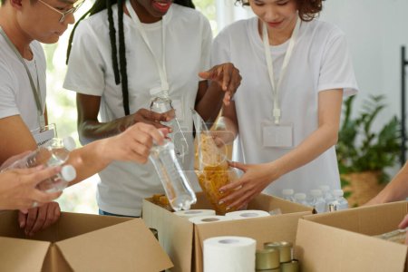 Téléchargez les photos : Organismes caritatifs qui mettent des emballages de macaronis et d'eau embouteillée dans des boîtes en carton - en image libre de droit