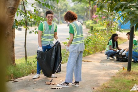 Photo for Young couple volunteering in public park on weekend, collecting garbage - Royalty Free Image