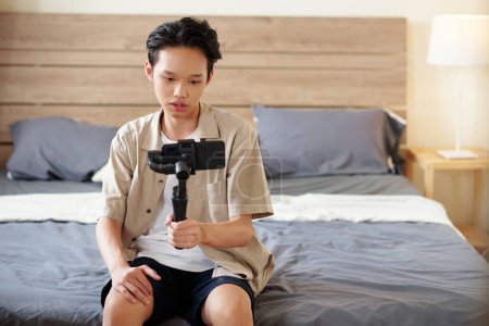 Foto de Adolescente niño sosteniendo smartpone unido a monópodo al grabar video blog - Imagen libre de derechos