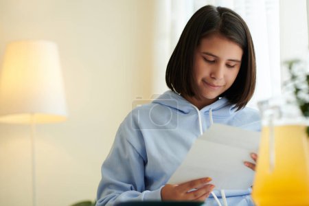 Photo for Smiling teenage girl reading letter she received from college - Royalty Free Image