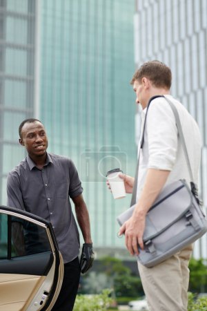 Photo for Positive taxi driver greeting and opening door for passenger - Royalty Free Image