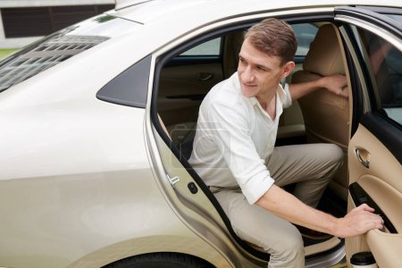 Photo for Entrepreneur opening car door and getting out of taxi at office building - Royalty Free Image