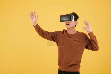 Téléchargez les photos : Jeune homme en sweat-shirt marron jouant au jeu vidéo en casque VR - en image libre de droit