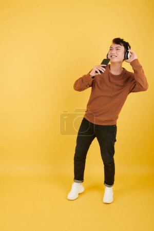 Téléchargez les photos : Joyeux jeune homme dans les écouteurs enregistrement drôle de message vocal pour son ami - en image libre de droit