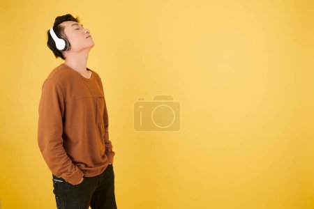 Téléchargez les photos : Jeune homme penché la tête en arrière en profitant de sa chanson préférée sur écouteurs - en image libre de droit