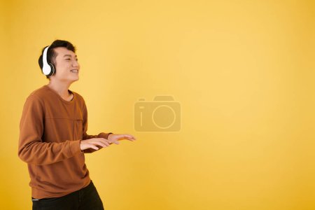 Téléchargez les photos : Jeune homme souriant dans un casque prétendant jouer du piano invisible - en image libre de droit