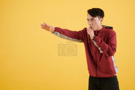 Foto de Entrenador frunciendo el ceño silbando y haciendo gestos con la mano, aislado en amarillo - Imagen libre de derechos