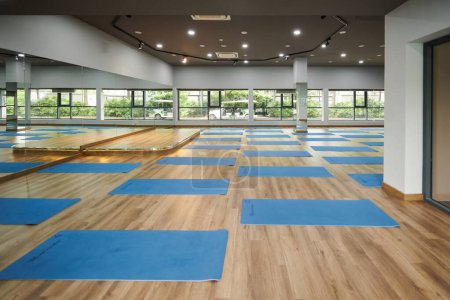 Téléchargez les photos : Tapis de yoga bleu déroulés dans un studio de danse vide spacieux - en image libre de droit