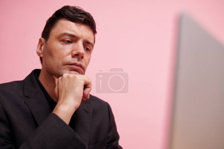 Téléchargez les photos : Homme d'affaires sérieux profondément dans ses pensées regardant l'écran d'ordinateur portable avec des données financières - en image libre de droit