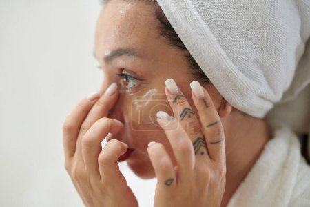 Photo for Girl with soft white towel on head putting under eye patch on her face after morning hygiene while standing in front of camera - Royalty Free Image