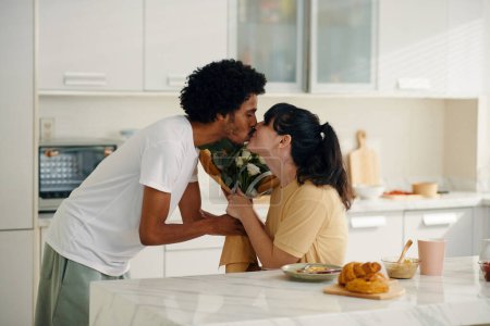 Téléchargez les photos : Jeune homme passant des fleurs à sa femme et l'embrassant sur les lèvres tout en félicitant son amour le jour de la Saint-Valentin - en image libre de droit