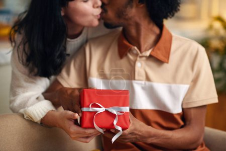 Photo for Hands of young affectionate husband and wife kissing each other while holding red giftbox with packed present for valentine day - Royalty Free Image