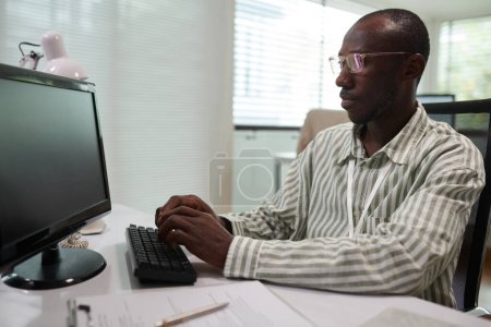 Téléchargez les photos : Portrait de sérieux développeur de logiciels noirs examinant le code de programmation sur l'écran d'ordinateur - en image libre de droit