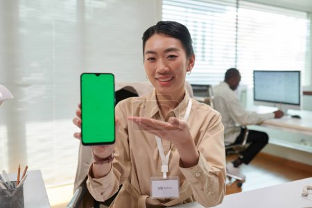 Photo for Portrait of smiling bank manager showing smartphone with green screen explaining how application works - Royalty Free Image
