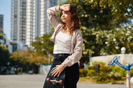 Téléchargez les photos : Portrait d'adolescente avec planche à roulettes debout dans le parc et regardant ailleurs - en image libre de droit